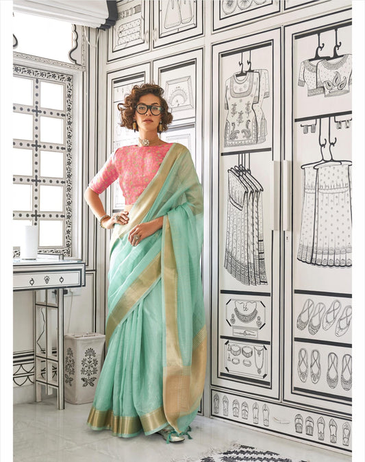 Woman in a teal saree with zari work standing in a room with black-and-white fashion illustrations on the walls