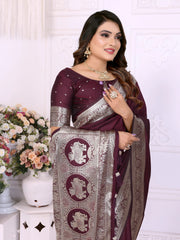 Woman wearing a wine-colored silk saree adorned with an elegant silver zari border and traditional elephant motifs on the pallu, paired with a matching blouse featuring silver detailing. She poses gracefully in a classic white floral-themed room decorated with ornate wall panels and flower arrangements in white vases.