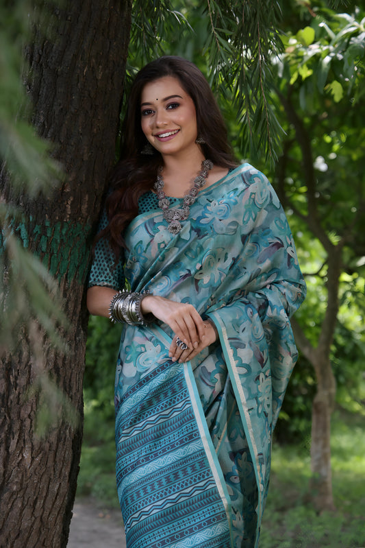 Woman wearing a blue floral silk saree with silver bangles, standing outdoors beside a large tree in a lush green garden

Woman wearing a blue floral silk saree with silver bangles, standing outdoors beside a large tree in a lush green garden.