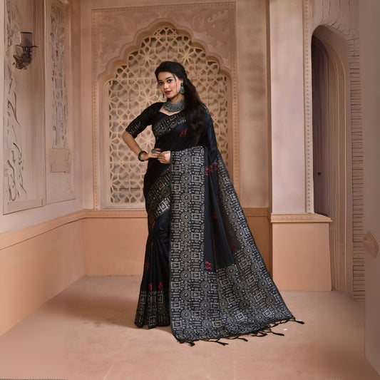Woman wearing a black silk saree with intricate geometric border and subtle red motifs, paired with traditional silver jewelry, standing in a heritage-inspired room with ornate lattice window and carved walls
