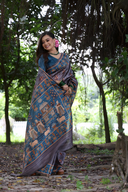 Woman wearing a grey silk saree with a blue border featuring traditional Pattachitra art and motifs, paired with green bangles and statement jewelry, standing on a leafy forest path under dense trees