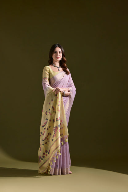  Woman wearing a lavender silk saree with a yellow floral pallu featuring tassel details, paired with a matching blouse and silver jewelry, standing against an olive green background.