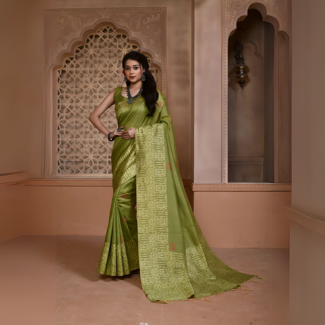 Woman wearing a light green silk saree with an intricate geometric border and pallu, paired with traditional jewelry, standing in a heritage-inspired room with ornate carved window and pastel walls