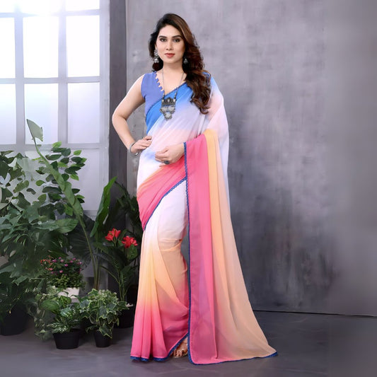 Woman wearing a multicolor gradient saree with blue blouse and statement necklace, standing indoors beside potted plants and a window with natural light.