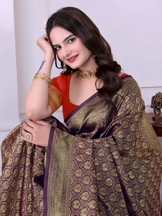 A woman models a striking Dark Brown Banarasi Silk Saree with dense all-over gold Zari weaving. The pallu provides a dramatic contrast in vibrant orange with heavy gold weaving. She wears an orange blouse and gold Kundan jewelry, posing indoors.