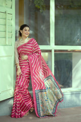 Woman wearing a pink silk saree with bold white geometric patterns and a floral embroidered pallu, accessorized with pearl jewelry and floral hair accessory, standing in a modern cafe interior near a window and glass table.