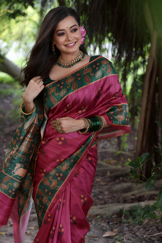  Woman wearing a pink silk saree with a green pallu featuring traditional motifs and gold jewelry, standing on a forest path surrounded by lush greenery