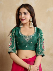 Woman wearing a royal purple silk saree with intricate pink and gold border and pallu, paired with a matching blouse and traditional gold jewelry, standing on a terracotta-tiled outdoor terrace with decorative plants and peach-colored walls