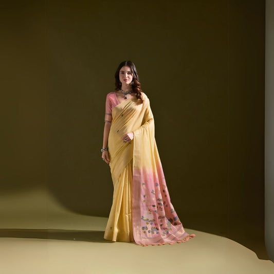  Woman wearing a yellow silk saree with pink floral print and matching pink blouse, standing against an olive green background.