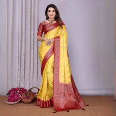Woman wearing a yellow silk saree with a rich maroon embroidered border and matching blouse, styled with traditional jewelry. She poses gracefully in a contemporary studio featuring baskets filled with rose petals and minimal decor, set against a neutral backdrop.
