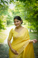Woman in yellow zari work saree walking on a garden path surrounded by green trees and grass